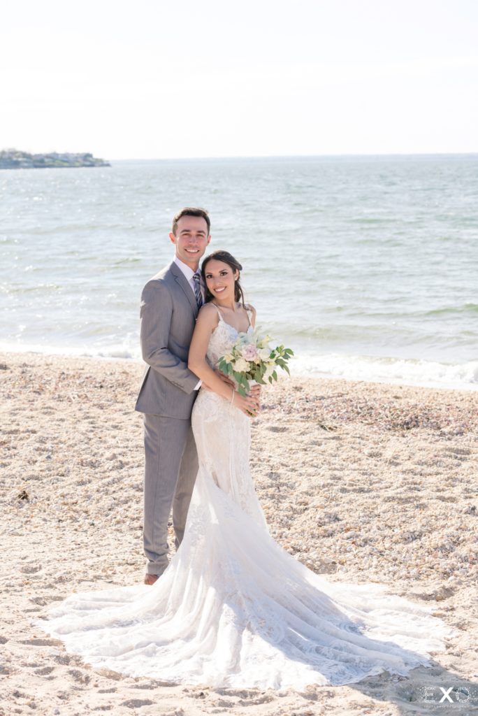 Bride and groom smiling by the shoreline.