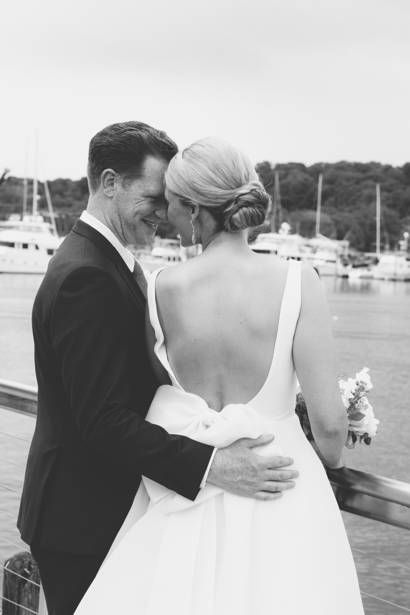 Black and white portrait of a bride and groom embracing at the harbor railing