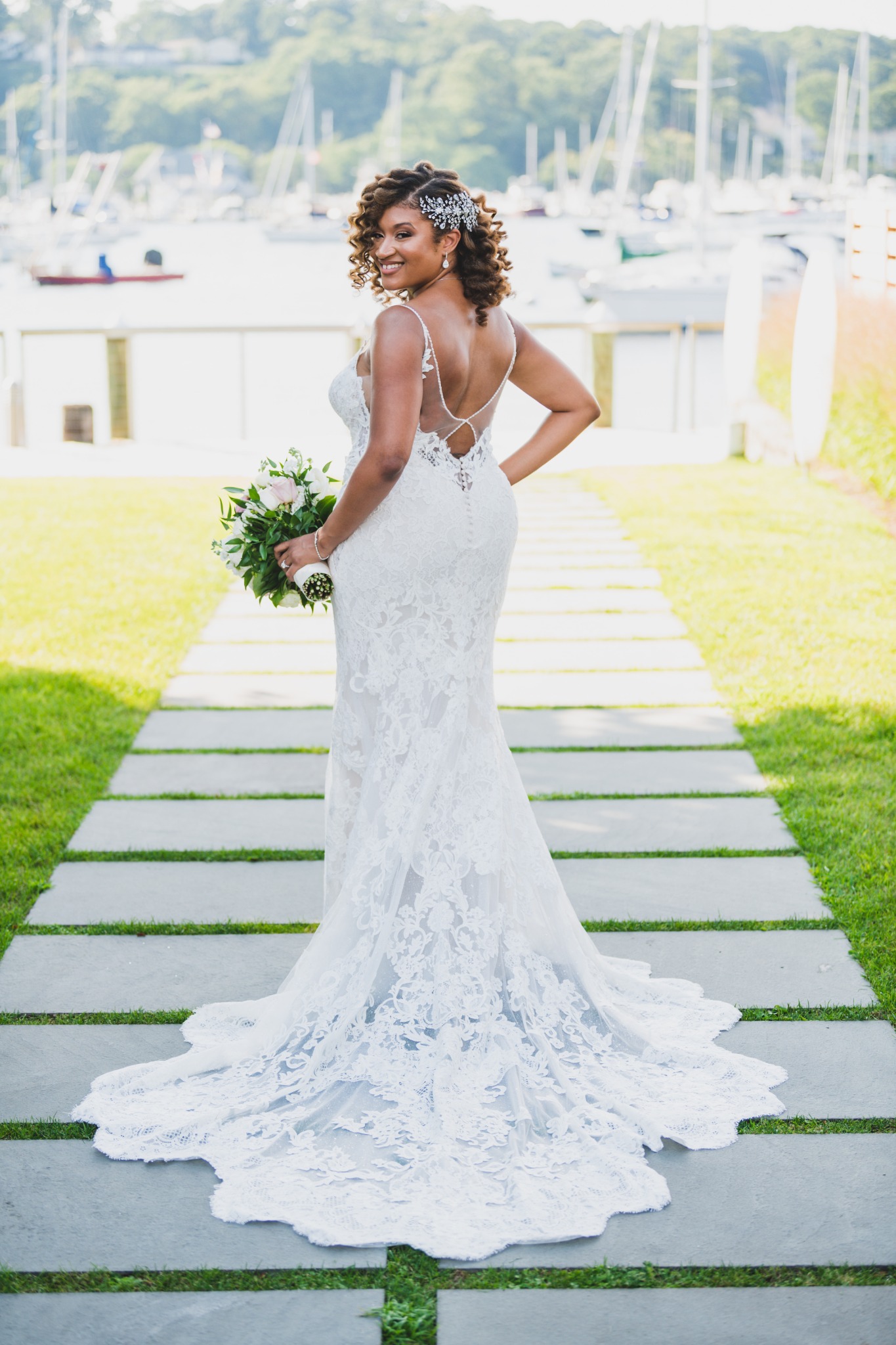 Bride posing on a waterfront garden walkway in a lace wedding gown
