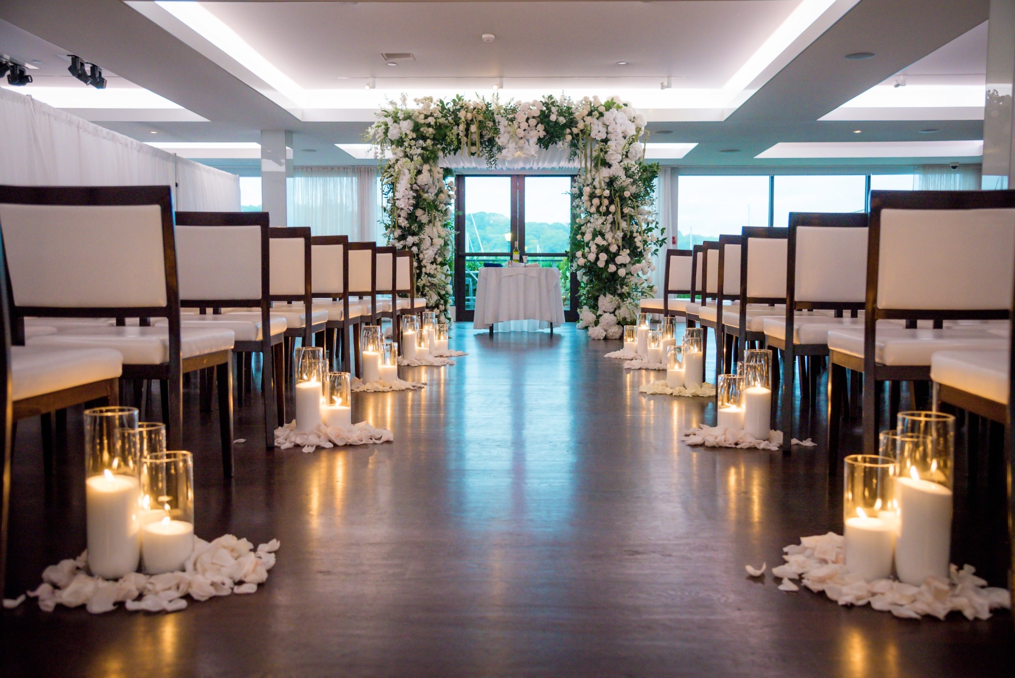 Indoor Harbor Club at Prime wedding ceremony with white floral arch, candles and rows of chairs