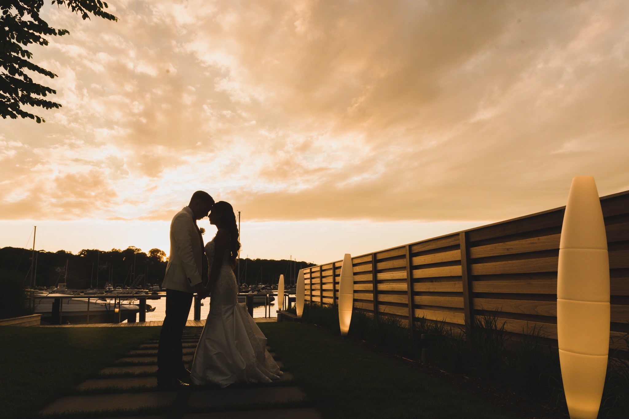 Bride and groom silhouetted against a golden sunset beside the marina