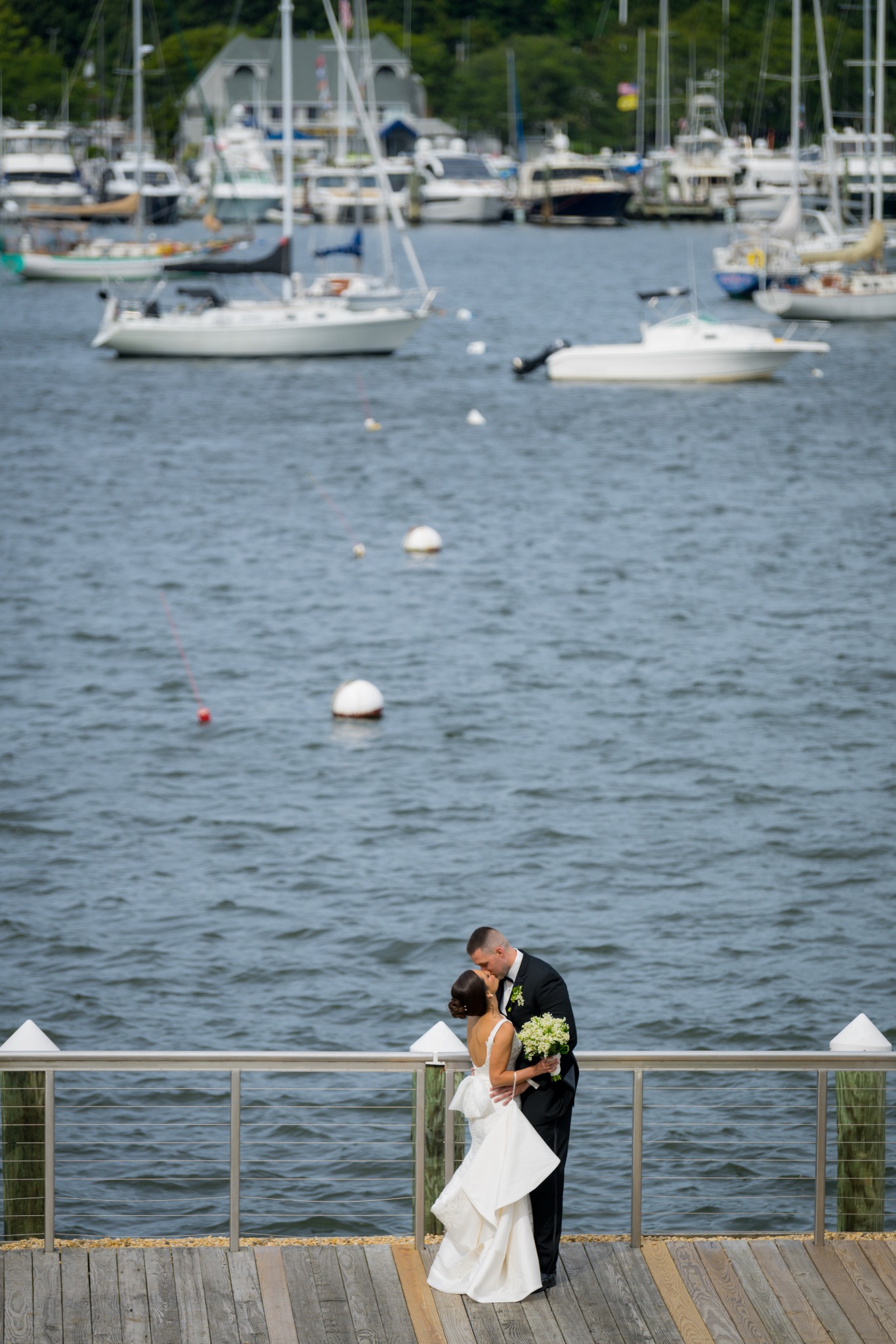 Newlyweds sharing a kiss in front of sailboats on the waterfront deck